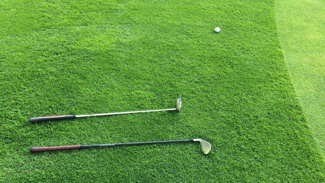 two golf clubs and a golf ball on a putting green