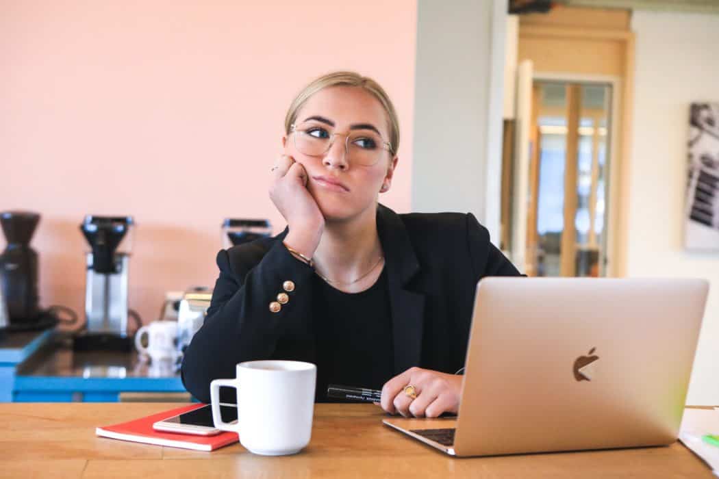 Blonde woman deep in thought sitting in front of a laptop at a desk