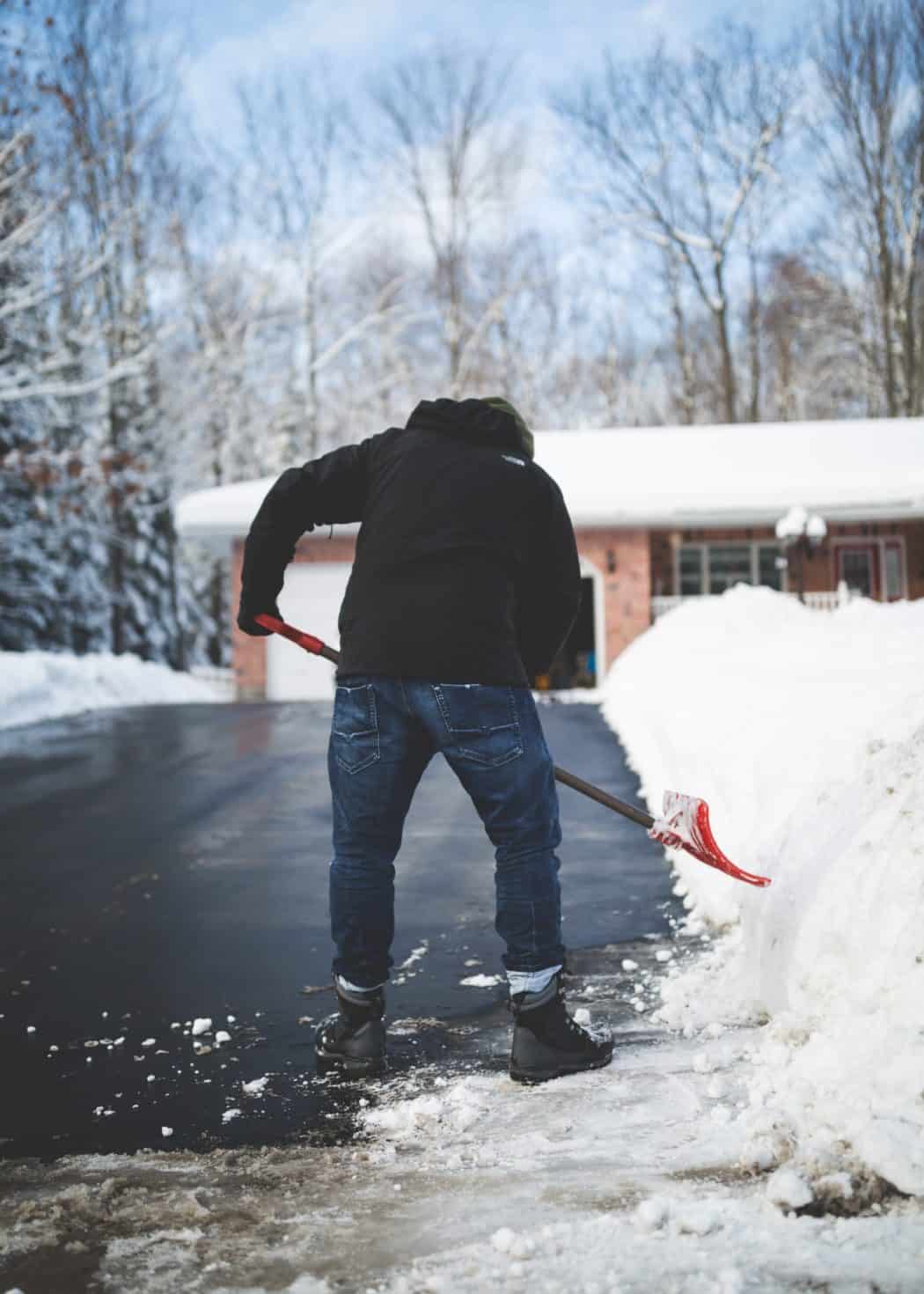 a homeowner in a sweatshirt shoveling a sidewalk after a fresh snowfall