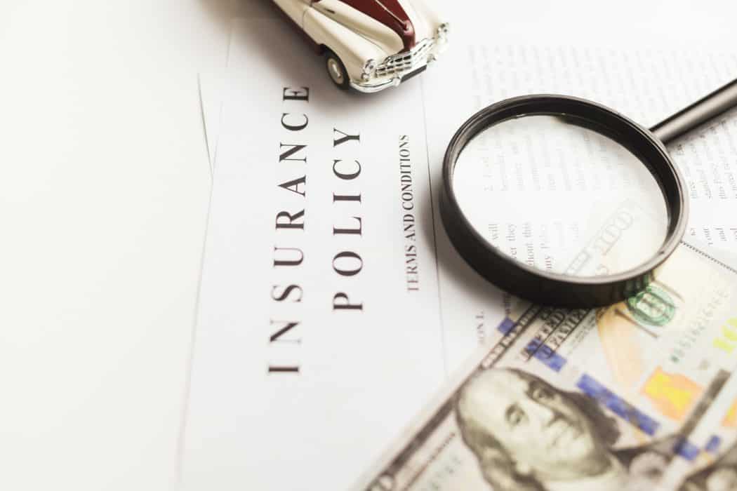 An insurance policy, magnifying glass and money on a table