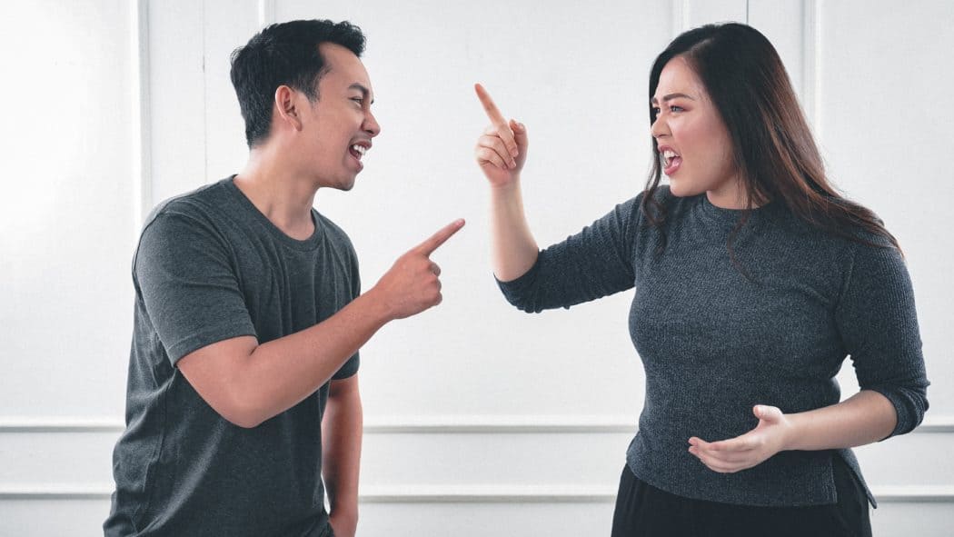 Romantic couple arguing, both wearing grey shirts and pointing fingers