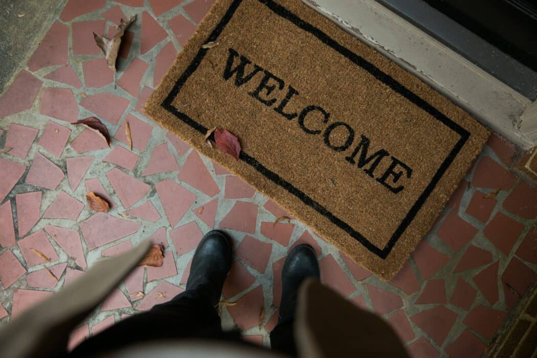 A person looking down at a welcome mat on a brick porch