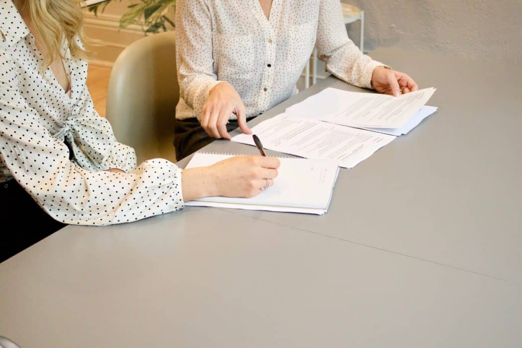 Two people sit at a table looking over a stack of papers